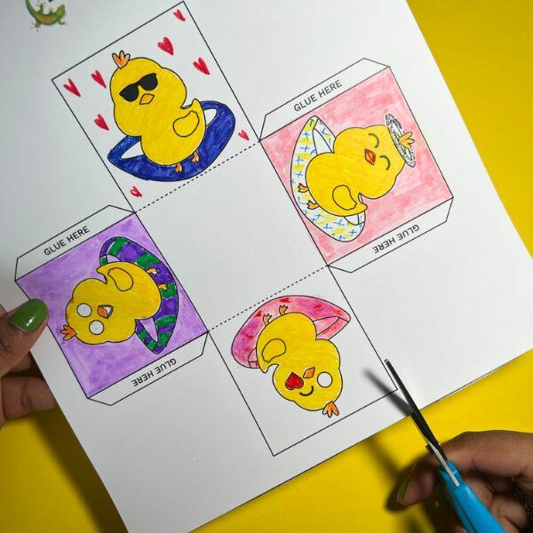 Hand using scissors to cut out a square panel of a chick from the coloured basket template.
