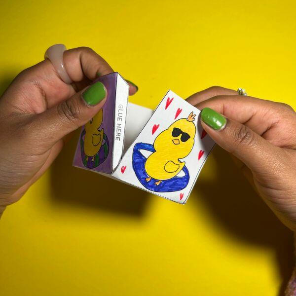 Hands folding and assembling two chick-decorated sides of the paper Easter basket.