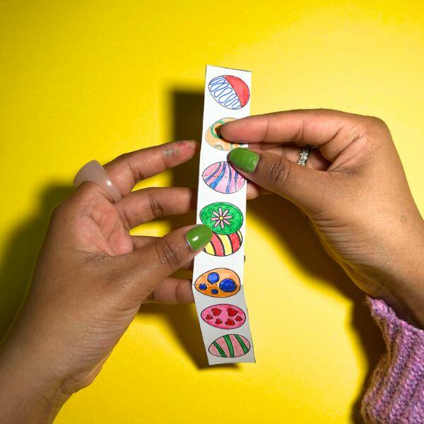 Hands holding a colourful handle decorated with Easter eggs for the basket.