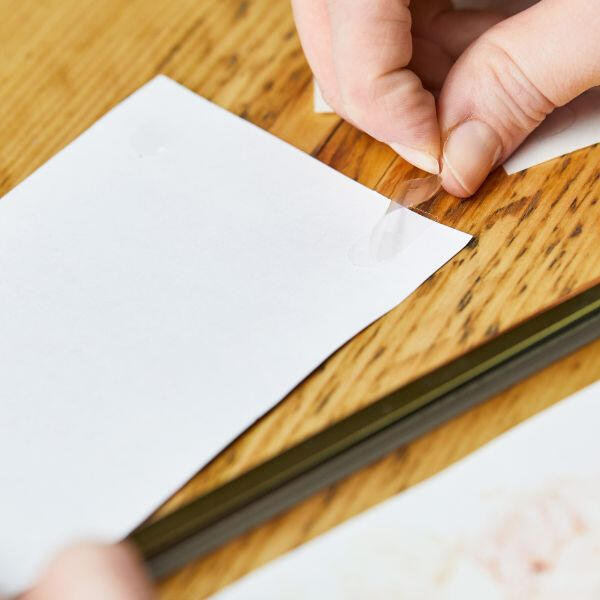 Fixing a white sheet of paper to a wooden table using a transparent sticky dot