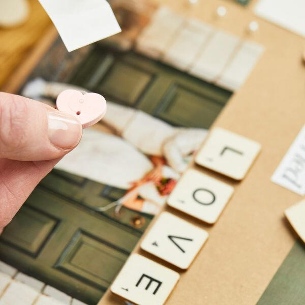 Holding a pink heart-shaped embellishment with sticky dot backing over a wedding photo collage