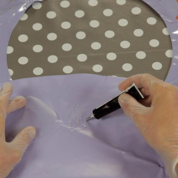 Person wearing gloves applying Bostik Soft Plastic Glue onto a patch area of a purple inflatable ring