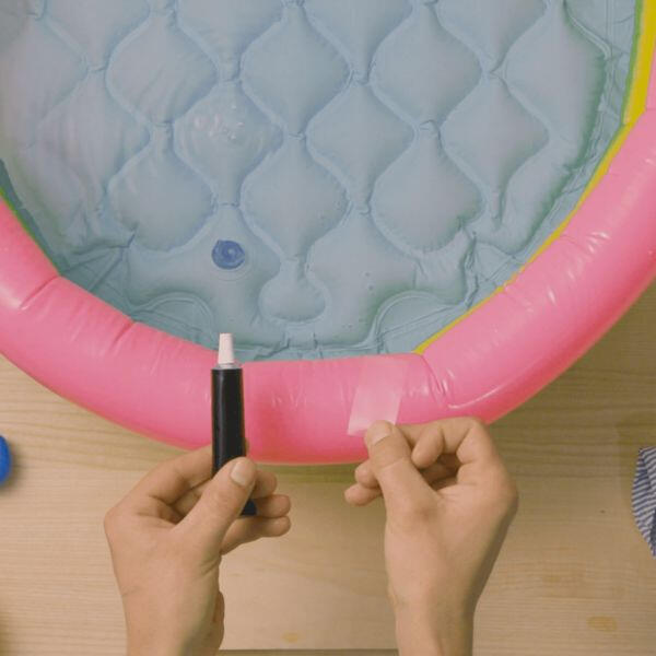 Hands squeezing Bostik Soft Plastic Glue onto a wooden surface in preparation for application, with a pink inflatable pool in the background.