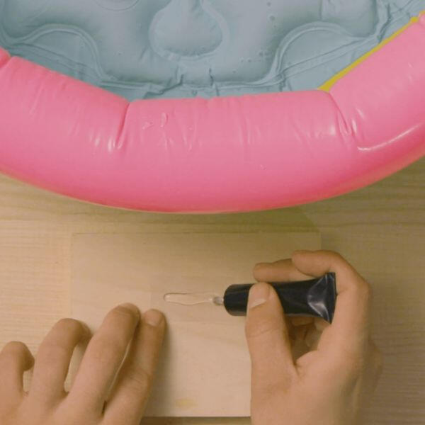 Hands squeezing Bostik Soft Plastic Glue onto a wooden surface in preparation for application, with a pink inflatable pool in the background.