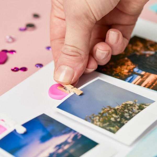 Hands pulling and stretching a piece of pink Blu Tack Colour on a pink background with scattered sequins.