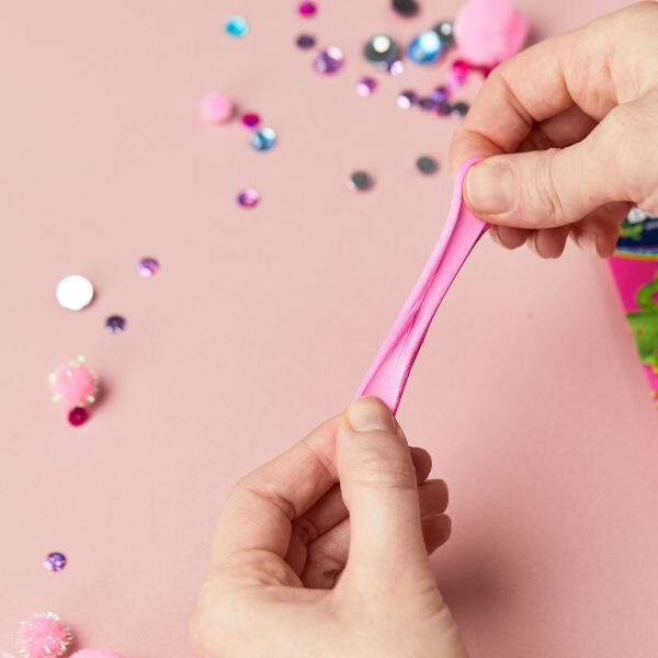 Hand pressing a small wooden clip into pink Blu Tack Colour to hold photographs on a scrapbook page.