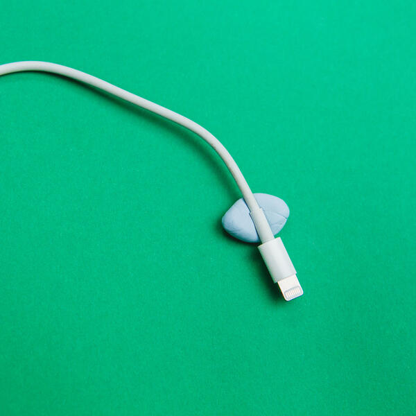 Bostik Blu Tack securing a white cable on a green surface for cable management.
