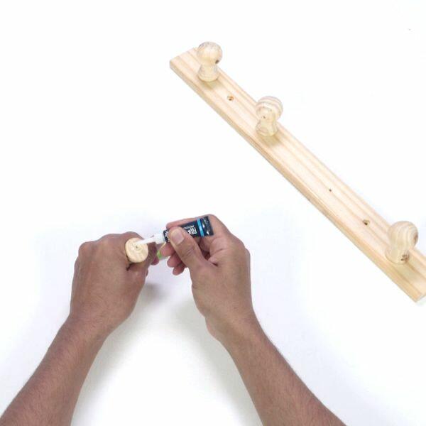 Applying super glue to the detached wooden peg in preparation for reattachment to the coat rack.