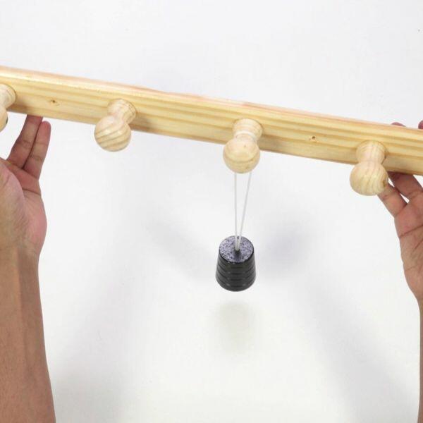 Wall-mounted wooden coat rack shown fully assembled with four pegs and a hanging weight, demonstrating durability after repair.
