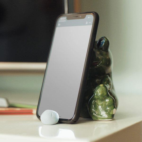 Smartphone propped up with Bostik Blu Tack and a green frog figurine on a desk.