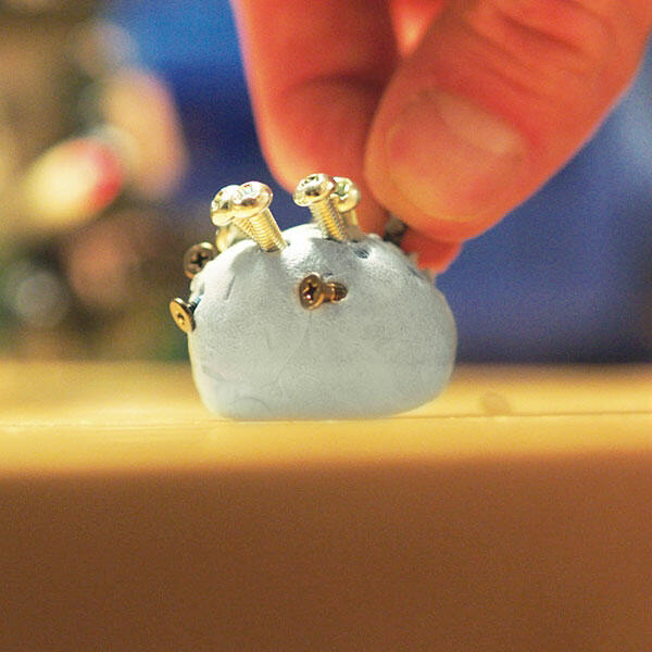 Hand placing a screw into Bostik Blu Tack to hold hardware during a DIY project.