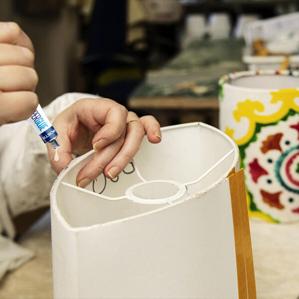 Applying Bostik Super Glue Liquid to repair a white lampshade frame.