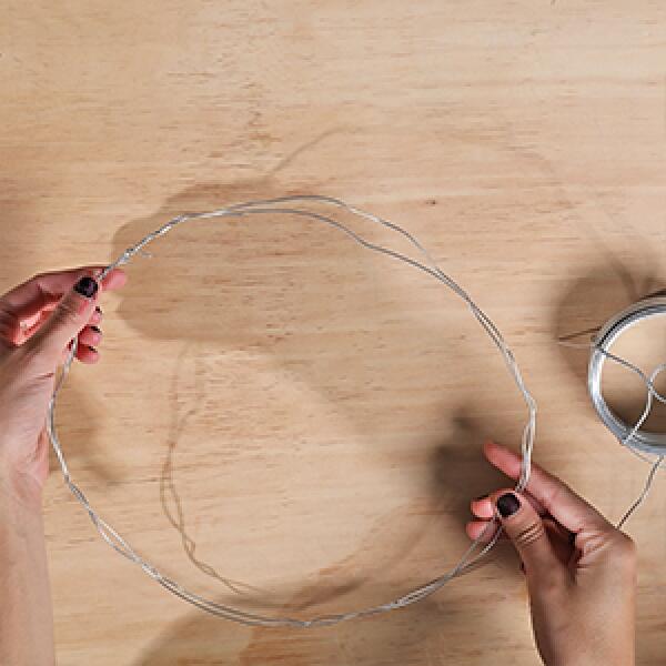 Hands shaping a circular wire base on a wooden table to create the foundation for a DIY wreath.