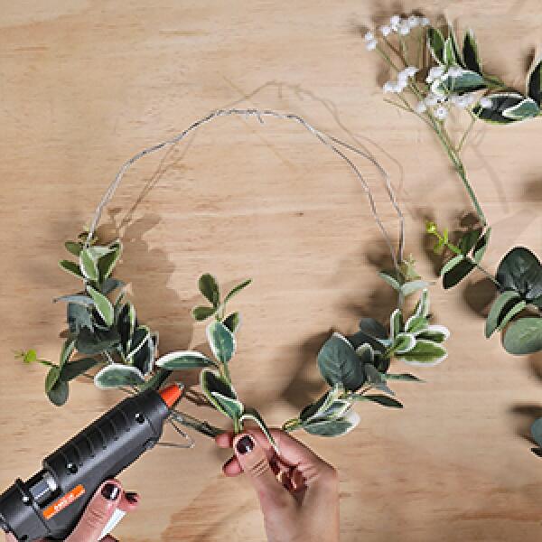 Attaching green leaves to the wire frame with a hot glue gun to start building the wreath.