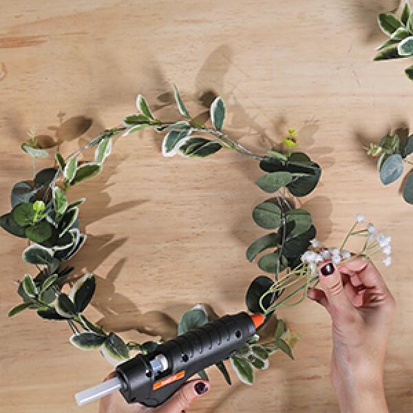 Adding more greenery and small white flowers with hot glue to fill out the DIY wreath frame.