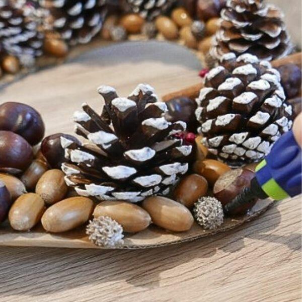 DIY wreath assembly with pinecones, twine, and dried berries placed on a cardboard ring, ready to glue.