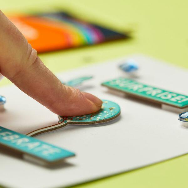 Finger pressing down on a card embellishment fixed with Bostik Foam Pads.