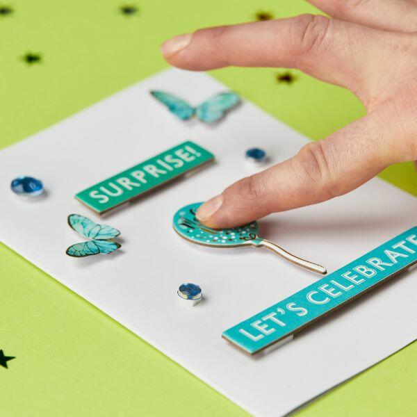 Attaching decorative shapes to a card using Bostik Foam Pads for a 3D effect.