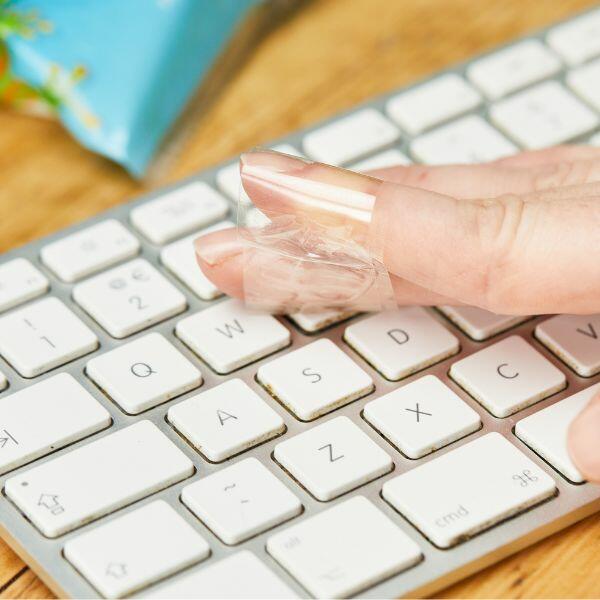 Using Bostik Sticky Tape to remove dust from a computer keyboard.