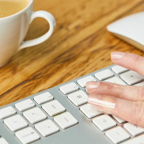 Finger using Bostik Sticky Tape to pick up debris between keyboard keys.