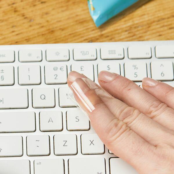 Cleaning a keyboard with a strip of Bostik Sticky Tape wrapped around fingers.
