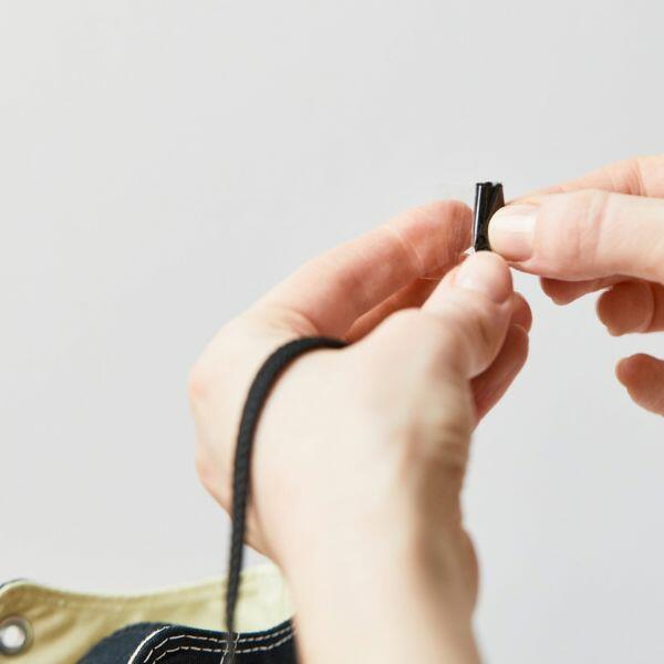 Wrapping tape around the end of a shoelace to repair a frayed tip.