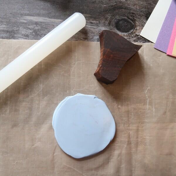 Roll out a flat circle of clay on a non-stick mat using a rolling pin, ready for stamping.