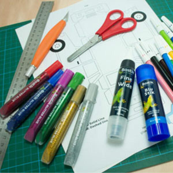 A printed yellow car template on white paper surrounded by markers, glitter pens, scissors, ruler, and Bostik glue sticks, ready to decorate.