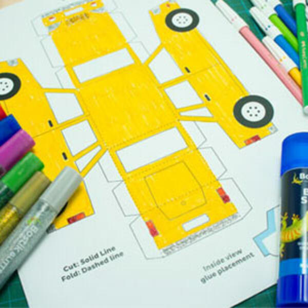 A yellow paper car template cut out and placed flat on a green cutting mat with an orange craft knife beside it.