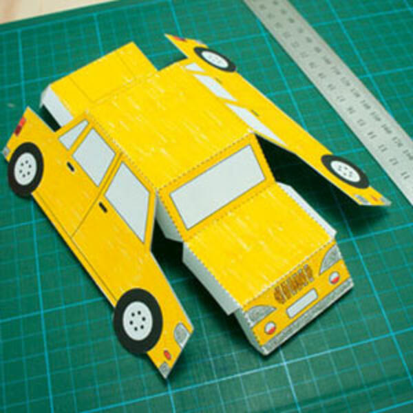 The folded car template forming the shell of the yellow car, with Bostik Fine & Wide glue nearby for assembly.