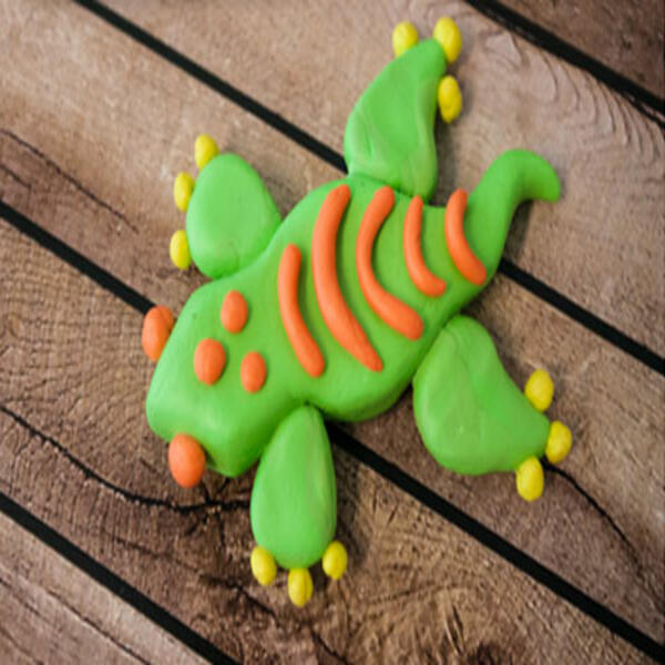 A nearly finished gecko made from green Blu Tack with bright orange stripes and yellow spots on its toes.