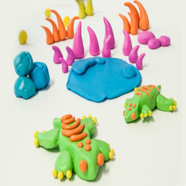 The completed Blu Tack gecko with orange stripes and yellow toes, displayed alongside colourful craft pieces.