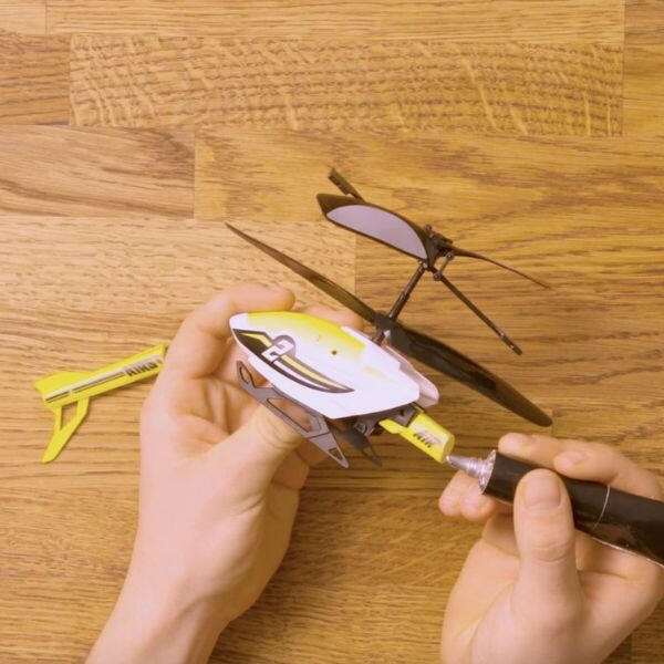 Bostik Hard Plastics Glue being applied to repair the tail of a small yellow and white toy helicopter on a wooden surface.