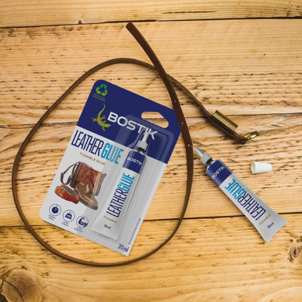Bostik Leather Glue tube and packaging placed next to a leather belt on a wooden surface, ready for repair.