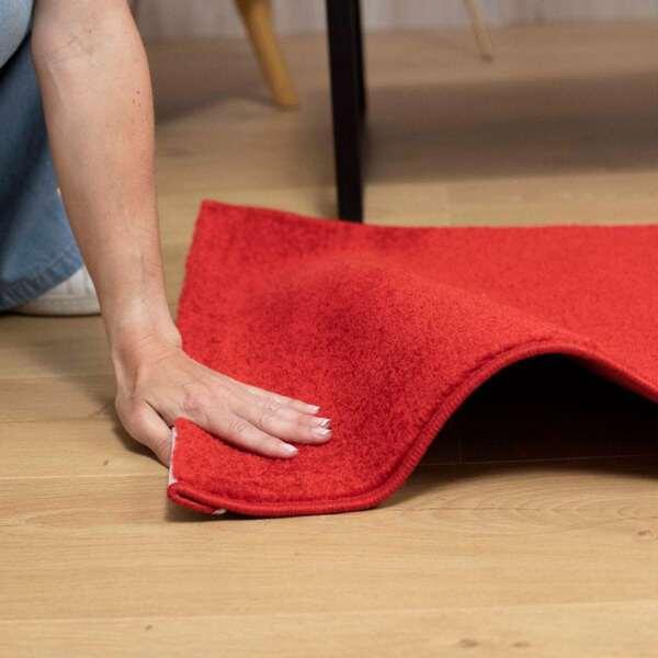 Hand securing a red rug to the floor with Bostik Miracle Mounting Tape for stability.